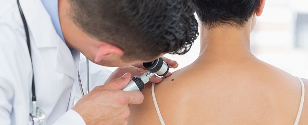 male dermatologist examining mole on back of woman in clinic